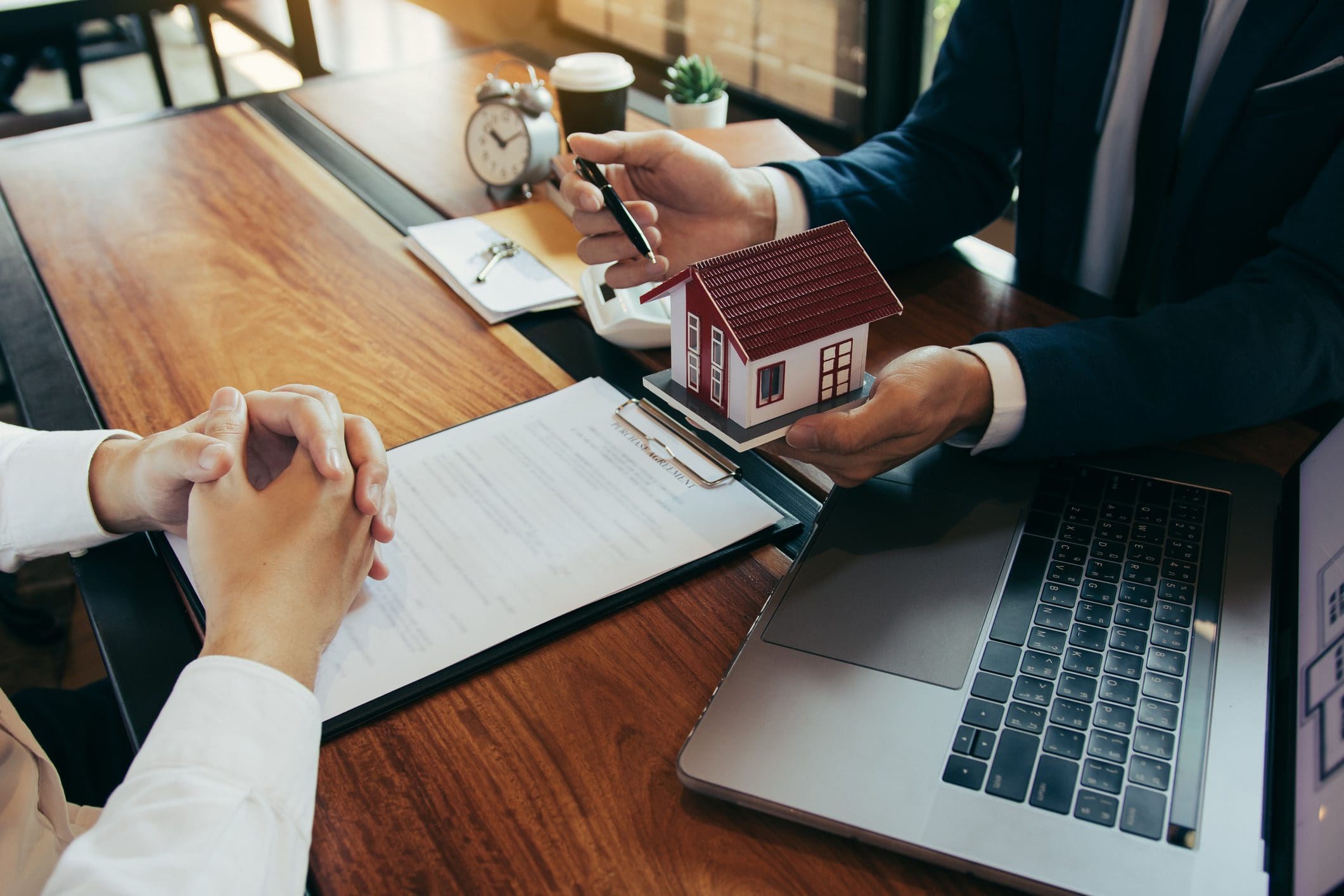 Real estate agent explaining house details to client with contract and laptop.