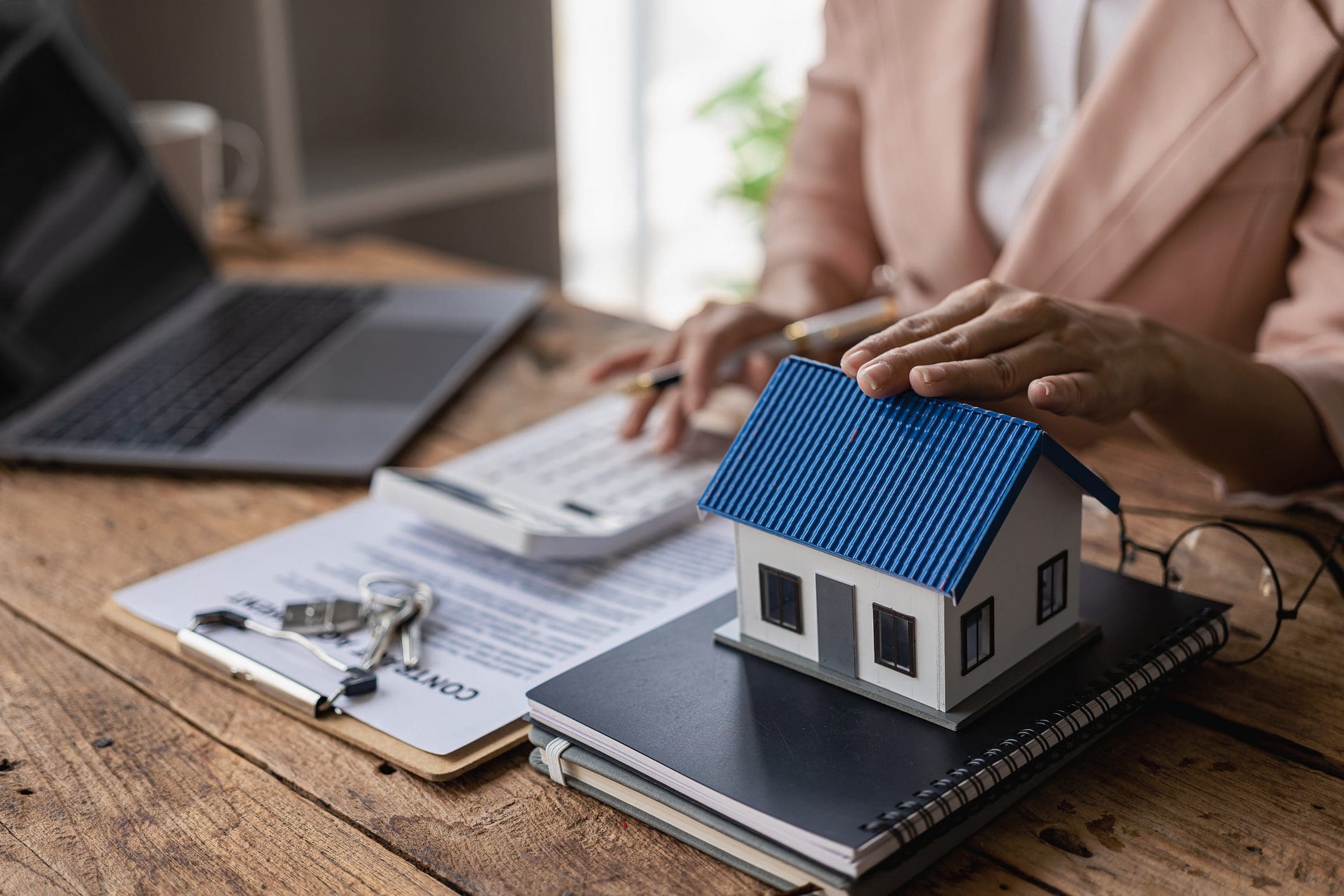 Person calculating finances with house model nearby.