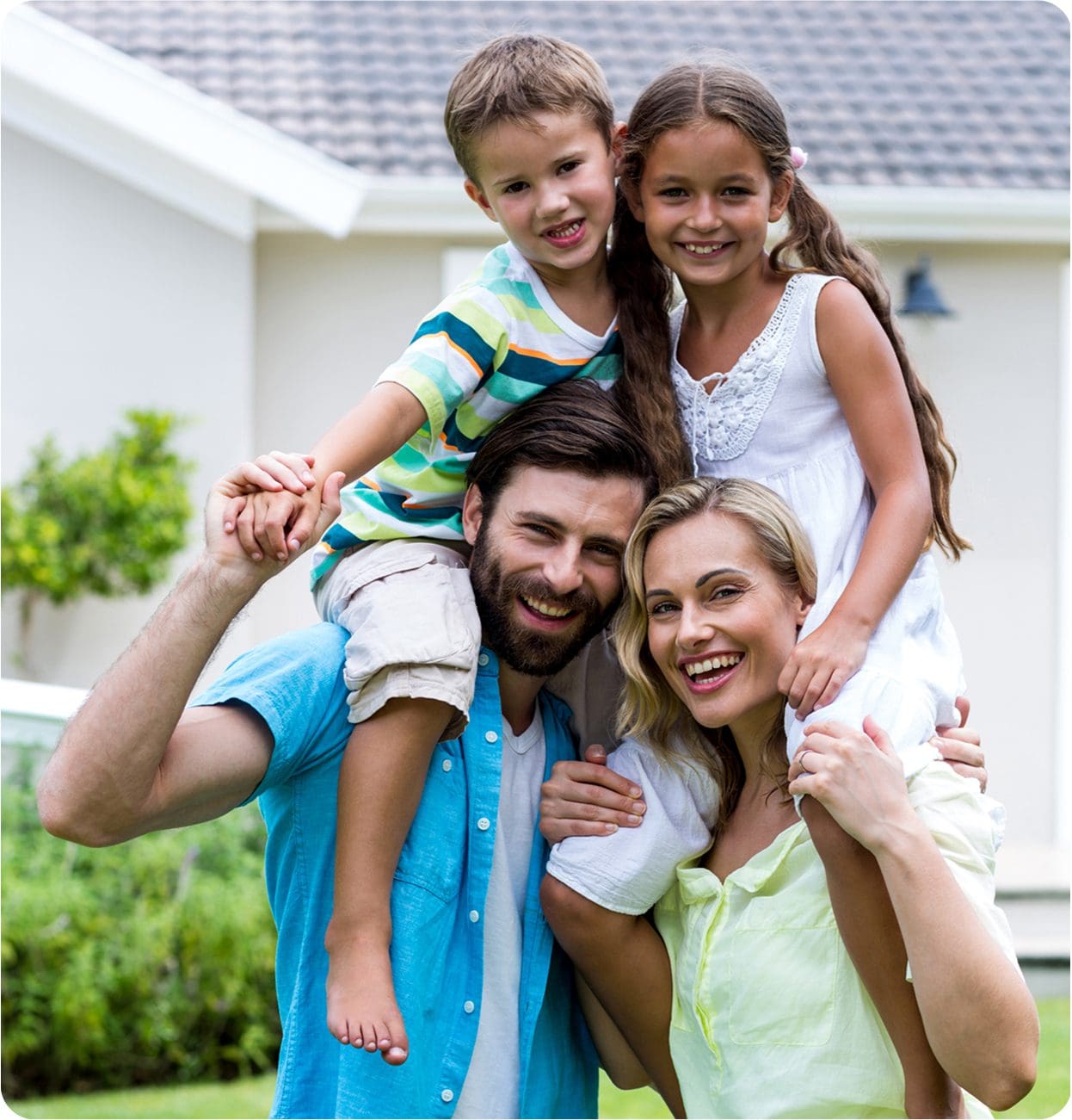 Happy family of four smiling outdoors in front of their home.